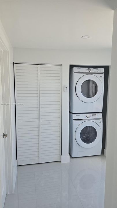 Laundry alcove featuring a stacked washer and dryer unit, floor-to-ceiling louvered-door closet, and large-format tile flooring