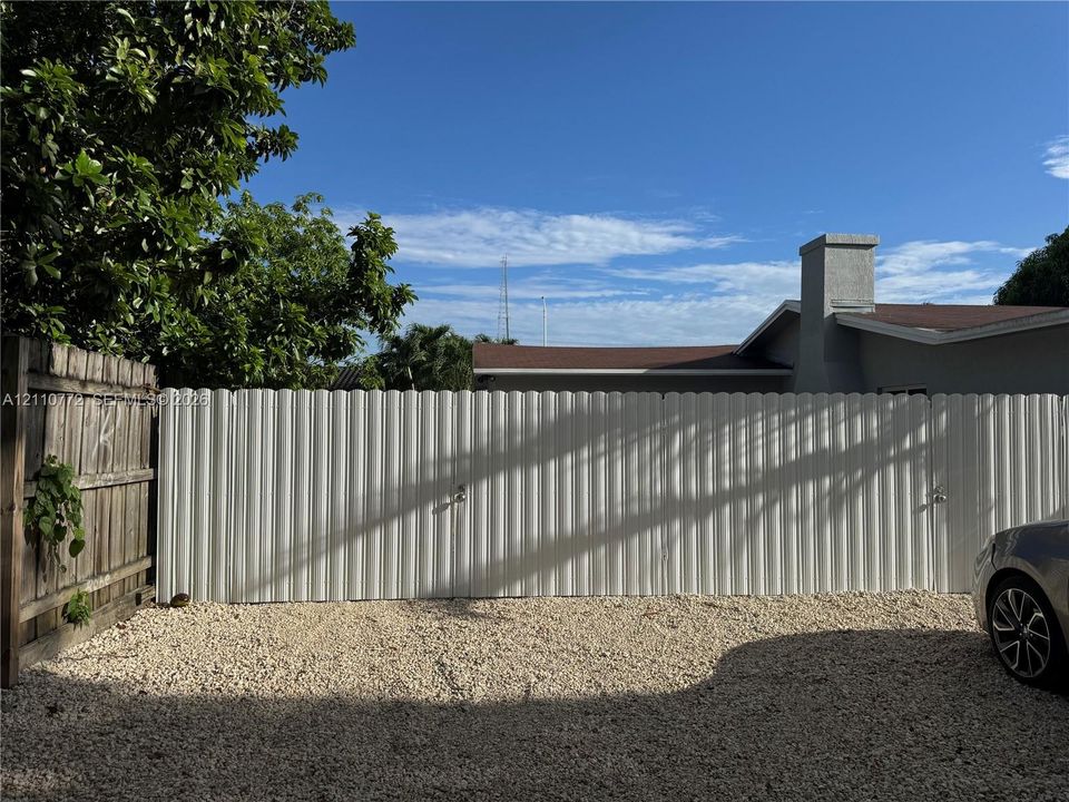 White corrugated privacy fencing with dual locking gates and gravel surface