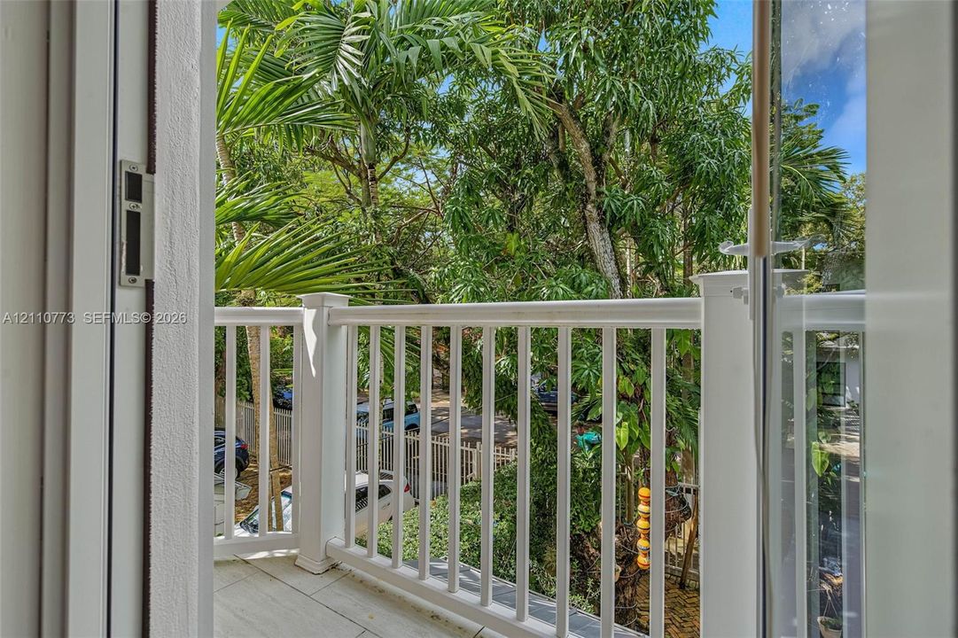 Covered balcony featuring white railings, neutral tile flooring, and mature palm tree canopy