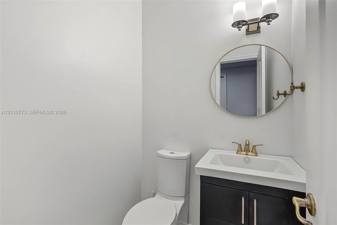 Powder room featuring a dark wood-finish vanity with a white integrated basin, metallic-finish faucet, wall-mounted circular mirror, and dual-light fixture