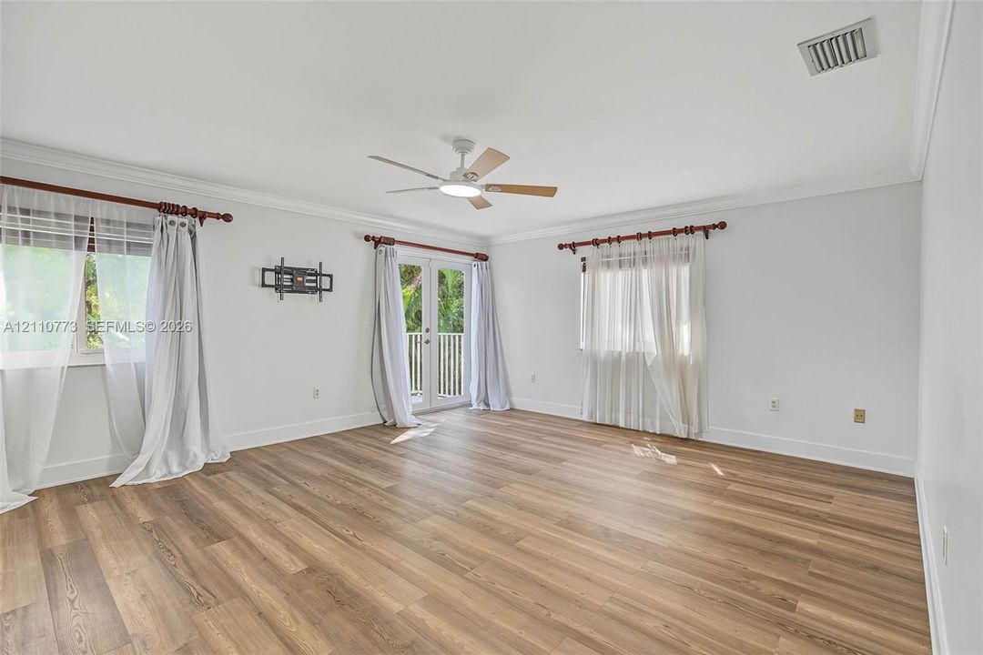 Spacious room featuring wood-finish flooring, crown molding, a central ceiling fan with integrated lighting, and glass-paned double doors