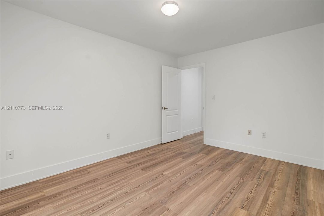 Interior room featuring wood-finish flooring, white walls, a flush-mount ceiling light, and a six-panel door with a metallic knob