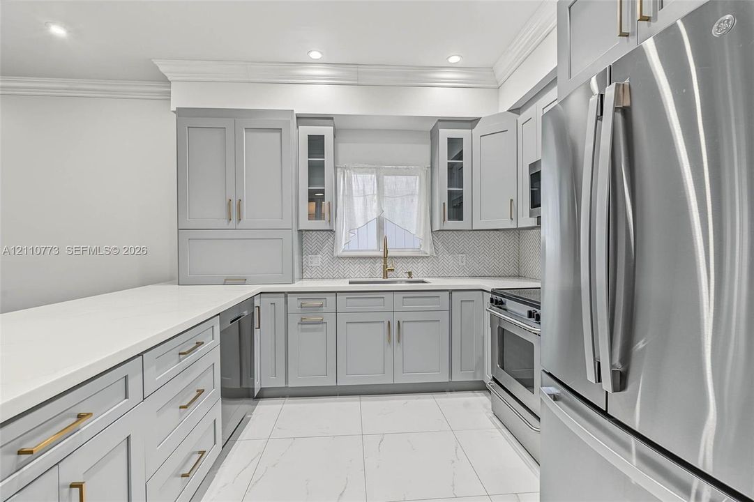 Kitchen featuring custom grey cabinetry, white quartz countertops, full-height hexagonal tile backsplash, stainless steel appliances, and large-format porcelain tile flooring