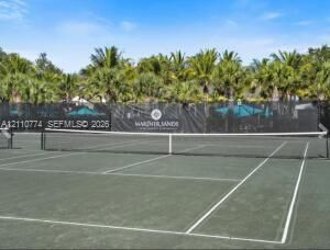 Tennis court featuring a hard surface, perimeter netting, and surrounding palm trees