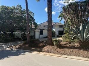 Multi-level exterior featuring stucco siding, a multi-gabled roofline, mature trees, and landscaping including agave and palm specimens