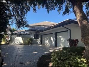 Exterior facade featuring a light-toned finish, multi-level roofline, multi-car garage with white doors, and a stone-paved driveway