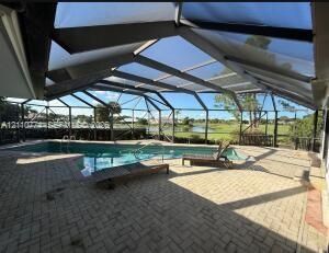 Screen-enclosed pool area featuring concrete paver patio, integrated swimming pool with ladder entry, and water backdrop