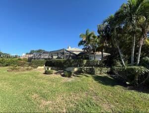 Expansive backyard featuring a manicured lawn, mature palm trees, perimeter shrubbery, and a screened-in lanai