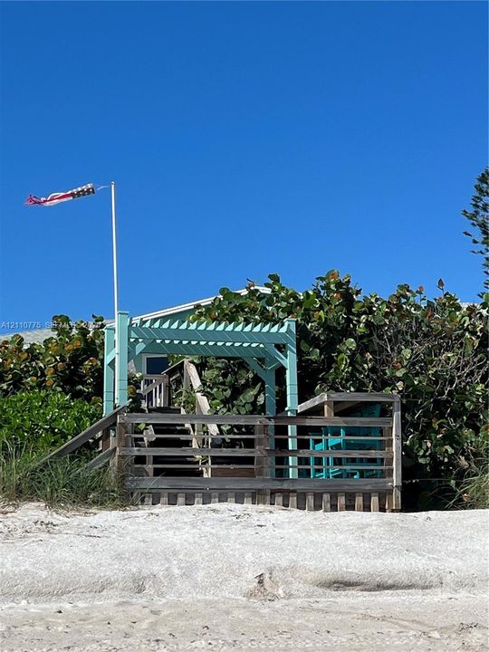 Coastal wood deck featuring a painted pergola, stair access, and integrated railing