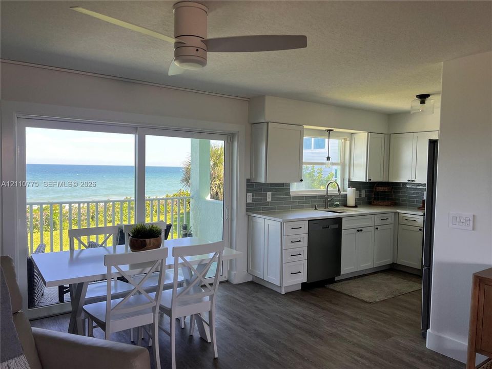 Kitchen featuring white shaker cabinetry, grey subway tile backsplash, solid-surface countertops, and wood-finish flooring, with sliding glass doors opening to an ocean backdrop