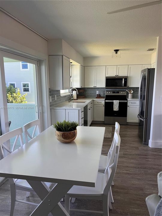 Kitchen featuring white cabinetry, solid-surface countertops, subway tile backsplash, stainless steel appliances, and wood-finish flooring