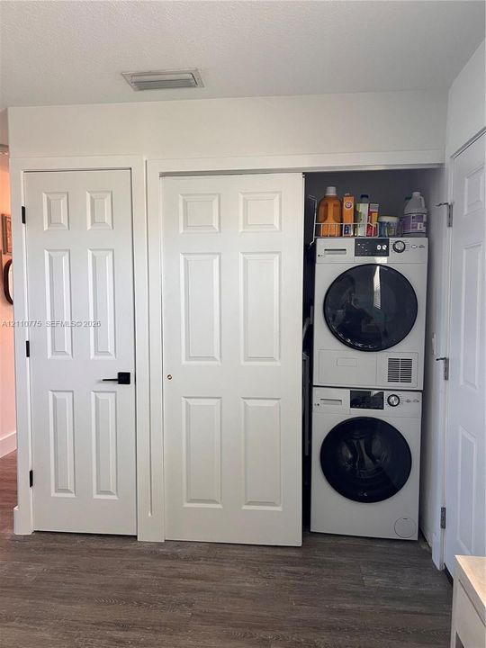 Laundry closet featuring stacked high-efficiency appliances, white paneled interior doors, matte black hardware, and wood-finish flooring