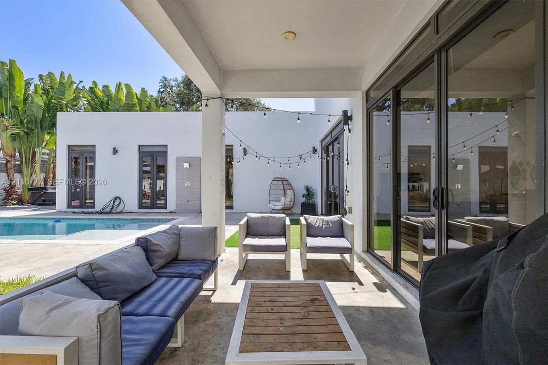 Covered patio featuring concrete flooring, sliding glass door systems, recessed ceiling lighting, and overhead string lights, situated near a swimming pool