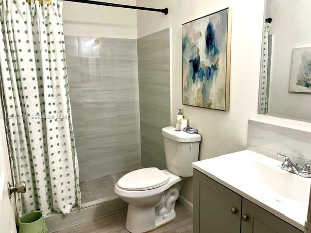 Bathroom featuring neutral-toned tile shower surround, grey vanity cabinet with integrated white countertop, and brushed metallic hardware