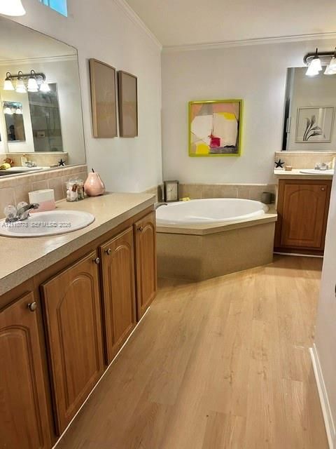 Dual vanity featuring stone-finish countertops with drop-in sinks, wood-finish cabinetry, an oval soaking tub with a tiled surround, and wood-finish flooring