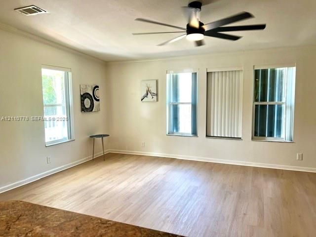 Living area featuring wood-finish flooring, a multi-blade ceiling fan with integrated lighting, and multiple windows providing natural light