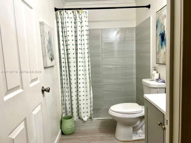 Bathroom featuring a walk-in shower with grey horizontal-tile surround, vanity with stone-top surface, and wood-finish flooring