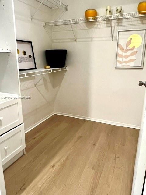 Walk-in storage space featuring wood-finish flooring, white built-in cabinetry with drawers, and wire shelving