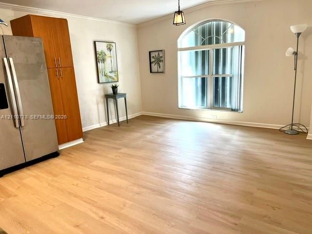 Light-toned wood-finish flooring, tall built-in wooden cabinetry, stainless steel refrigerator, and arched window with an integrated fanlight