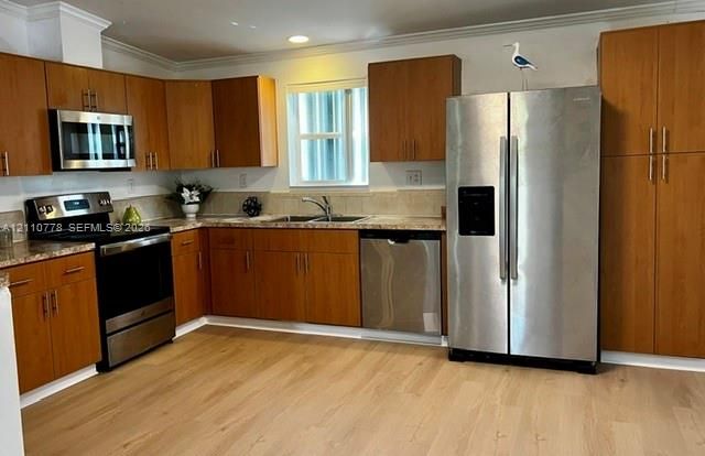 Kitchen featuring wood cabinetry, stainless steel appliances, stone-finish countertops, and wood-finish flooring