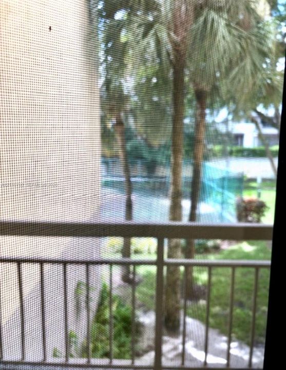 Balcony with metal railing and screen, featuring palm trees and a tennis court