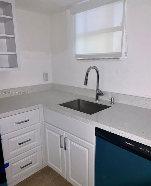 White shaker-style cabinetry with chrome hardware, stone-composite countertops, stainless steel undermount sink, high-arc chrome faucet, and integrated dishwasher