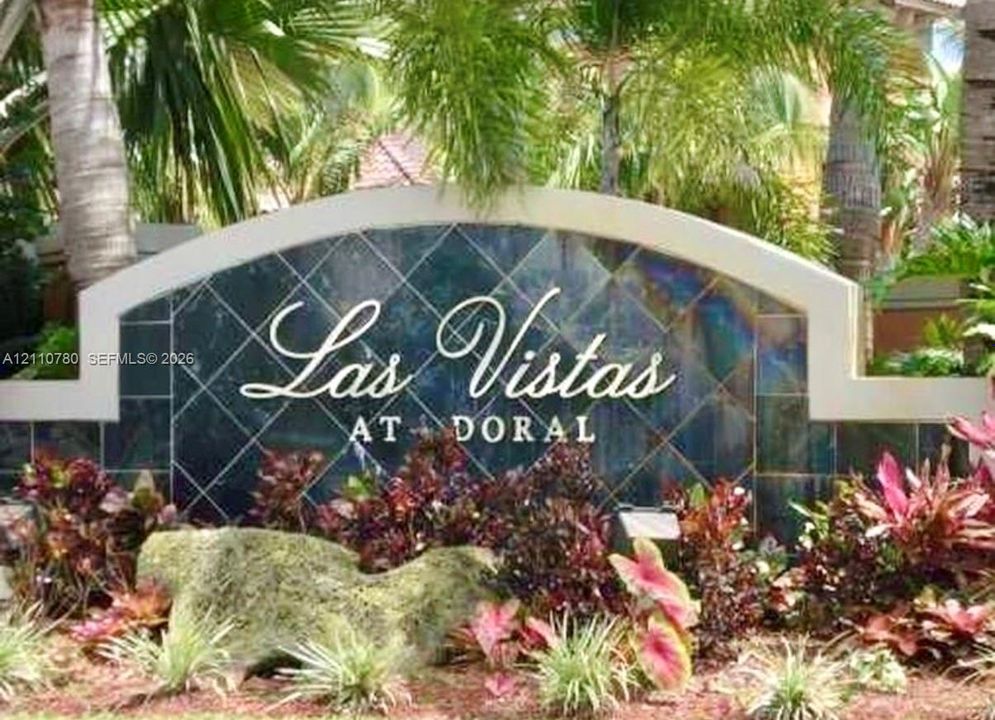 Las Vistas at Doral monument sign featuring custom arched masonry, dark glazed tile inlay, and professional landscaping with native tropical plantings and decorative stone boulder