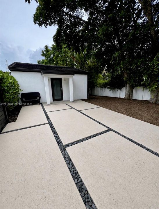 Concrete paver patio with dark stone inlay, stucco exterior finish, covered entryway, and mature trees