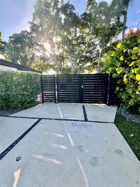 Horizontal slat privacy gate featuring matte black finish, accented by poured concrete pavers with stone-filled expansion joints and established perimeter shrubbery