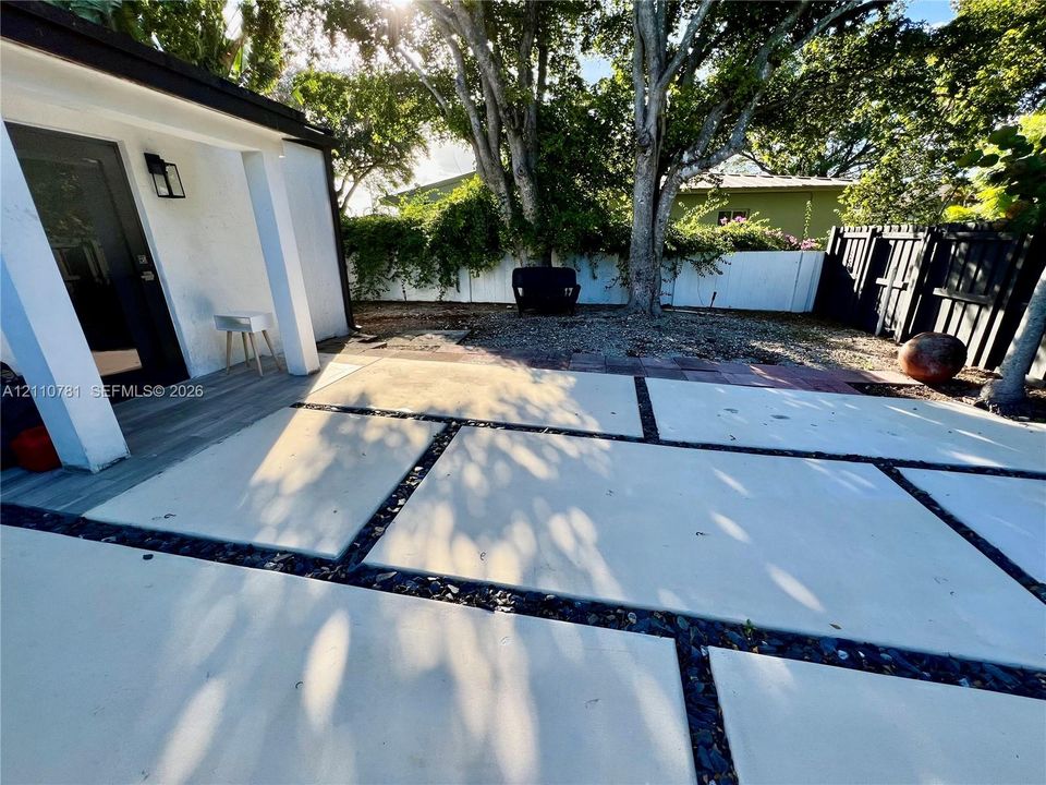 Rear patio featuring large-format concrete pavers with crushed stone borders and a white privacy fence