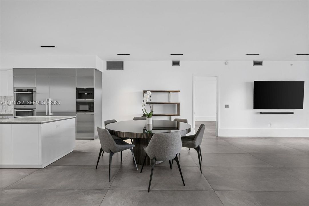 Open-concept space featuring large-format tile flooring, stainless steel integrated appliance suite, built-in shelving, and recessed ceiling lighting