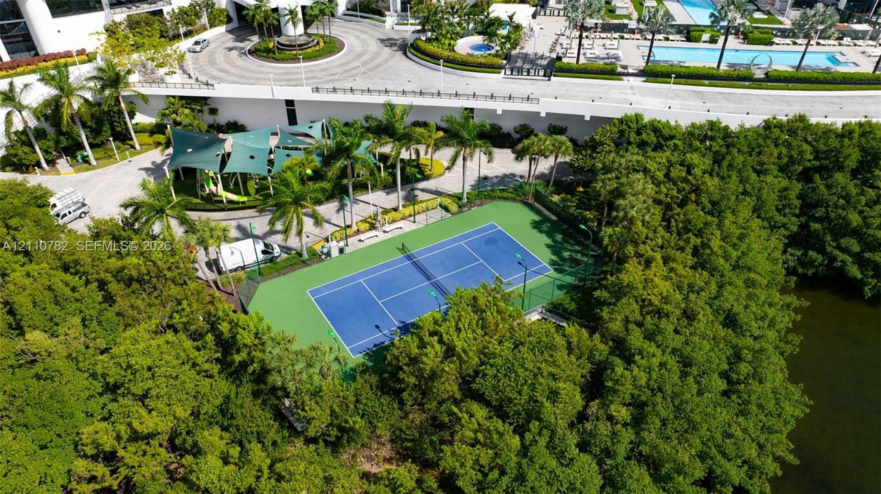 Tennis court with perimeter fencing, outdoor swimming pool, circular paved motor court, and canopy-covered recreation area
