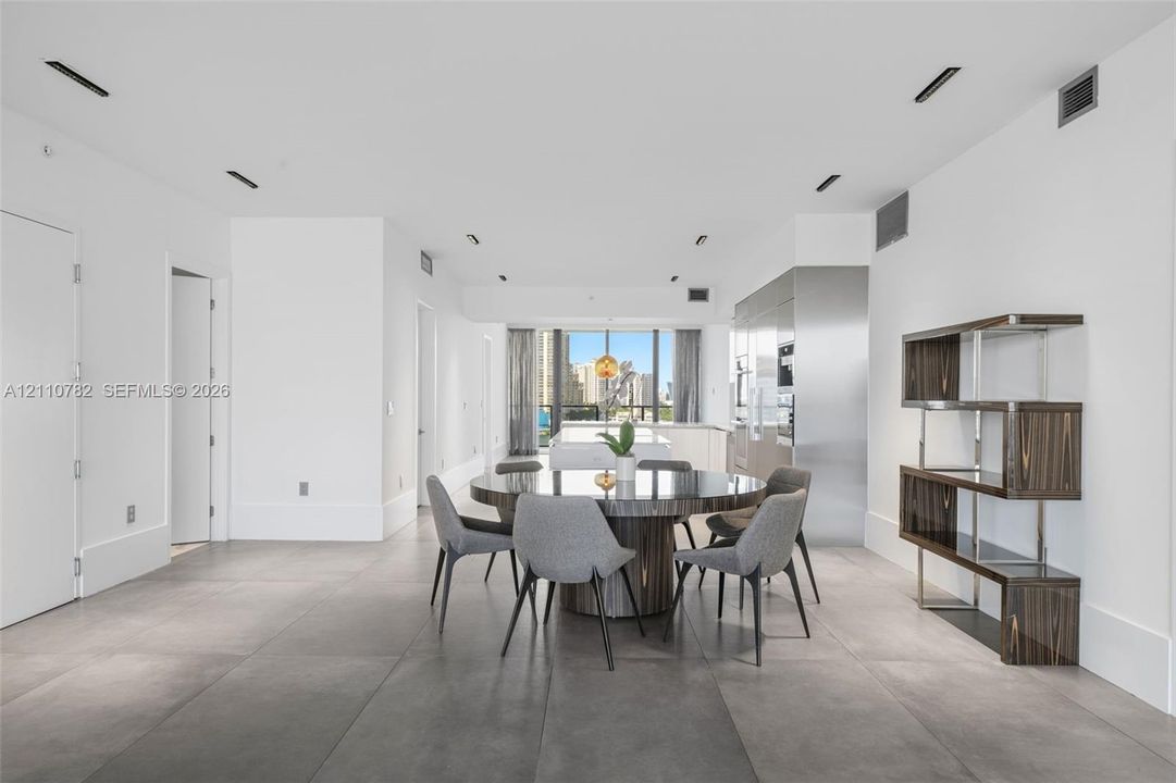 Open-concept space featuring large-format ceramic tile flooring, floor-to-ceiling windows, integrated stainless steel kitchen cabinetry, and recessed ceiling lighting
