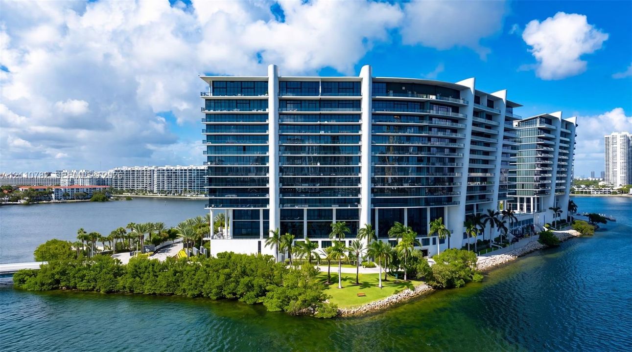 Multi-story waterfront high-rise featuring floor-to-ceiling glass windows, expansive private terraces, and extensive grounds with tropical landscaping