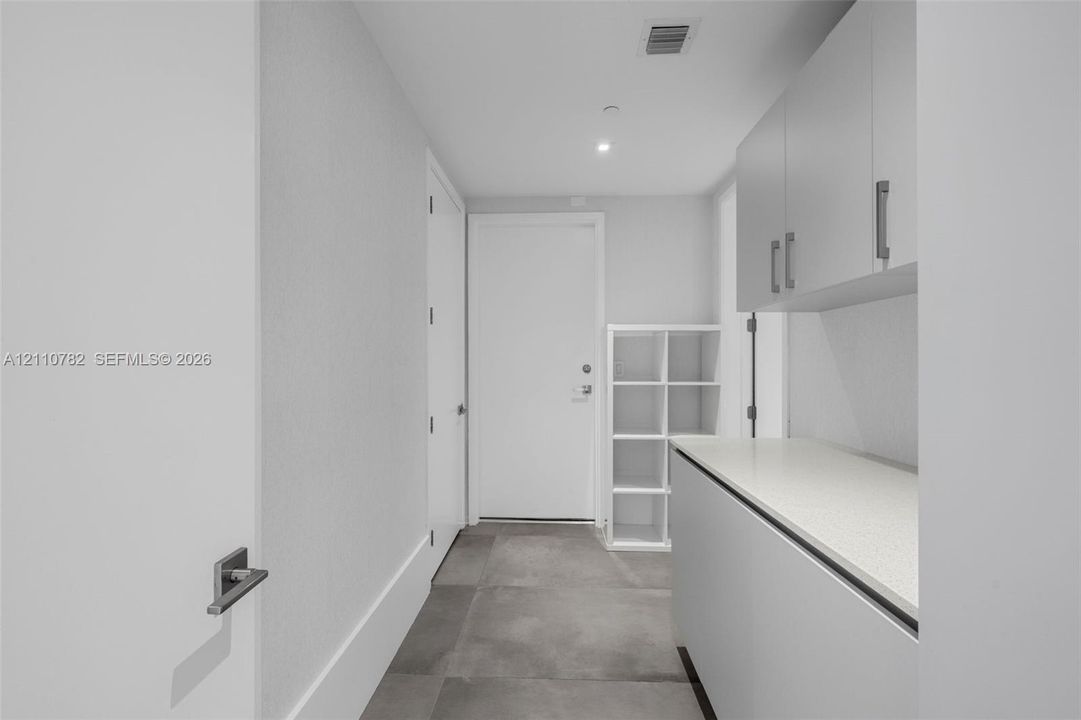Utility area featuring large-format tile flooring, built-in light-tone cabinetry, stone-composite countertops, and integrated storage shelving
