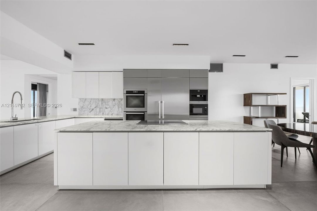 Contemporary kitchen featuring an expansive center island with stone surfacing, stainless steel built-in appliances, flat-panel cabinetry, a stone backsplash, and large-format floor tiling