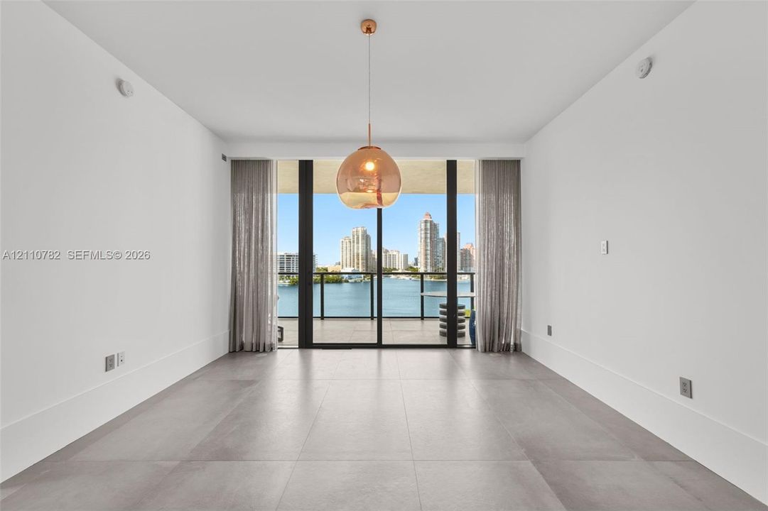 Large-format tile flooring, oversized sliding glass door, spherical glass pendant light, and balcony with water and city skyline backdrop
