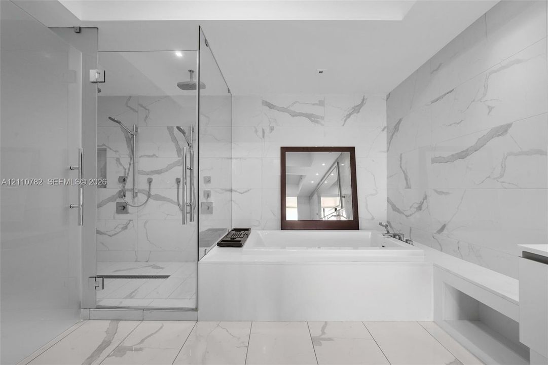 Large-format white tile with grey veining, glass-enclosed walk-in shower with rainfall showerhead, and a deep-soaking drop-in bathtub