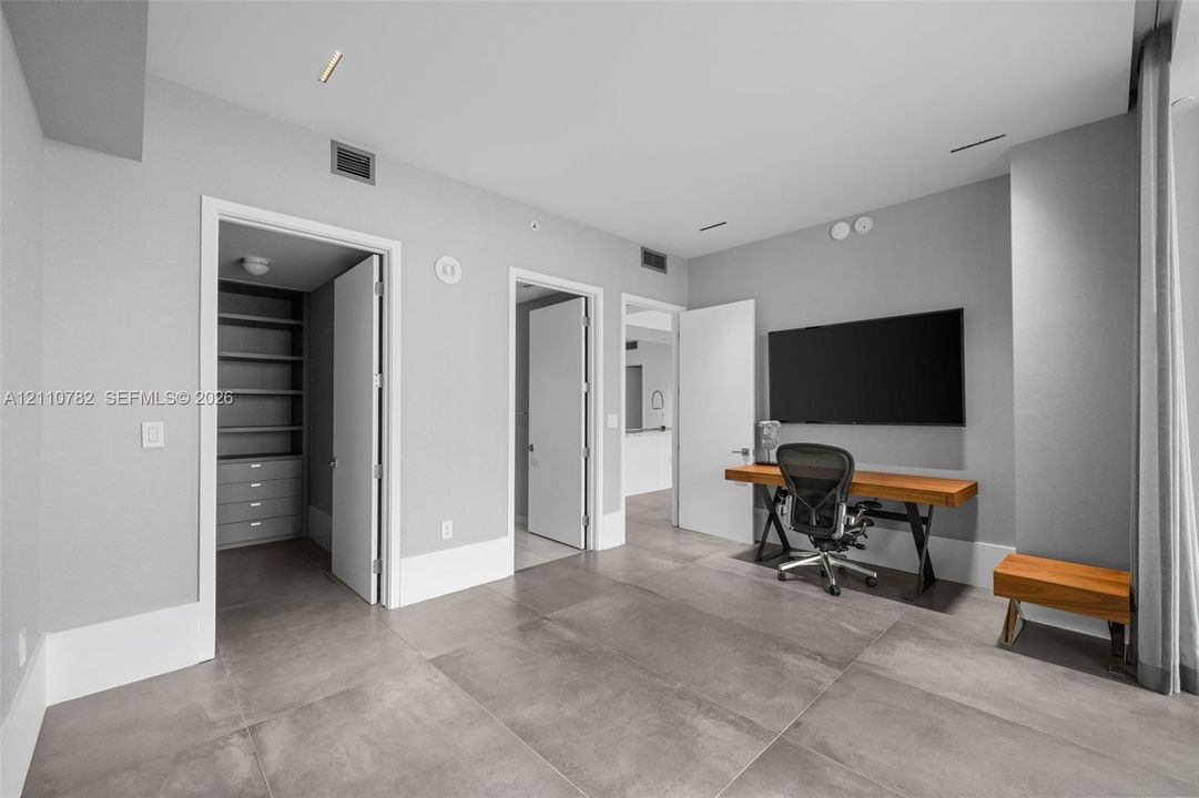 Large-format tile flooring, recessed ceiling lighting, and a walk-in closet featuring built-in shelving and integrated cabinetry