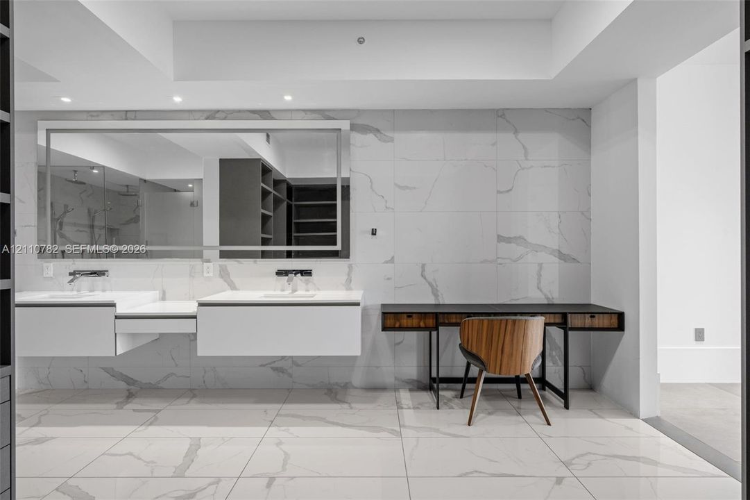 Floating dual vanity with integrated sinks, large-format stone-finish tile flooring and wall cladding, recessed lighting, and expansive wall-to-wall vanity mirror