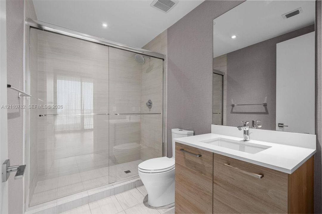 Bathroom featuring a glass-enclosed walk-in shower with tile surround, vanity with a light-tone wood finish, solid-surface countertop, and an integrated rectangular basin