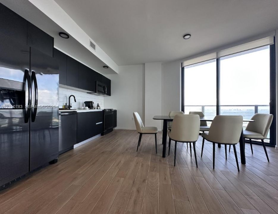 Kitchen featuring matte black cabinetry, white subway tile backsplash, wood-finish flooring, and floor-to-ceiling windows