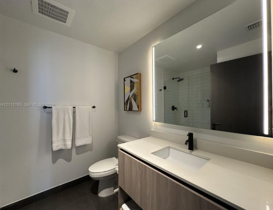 Floating vanity with wood-finish cabinetry, white countertop, rectangular under-mount sink, LED-backlit mirror, and matte black fixtures