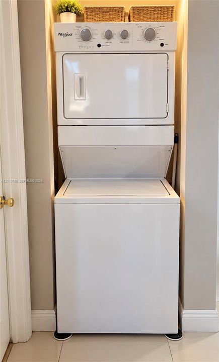 Stacked Whirlpool laundry center with neutral-toned walls, recessed alcove, and hard-surface flooring