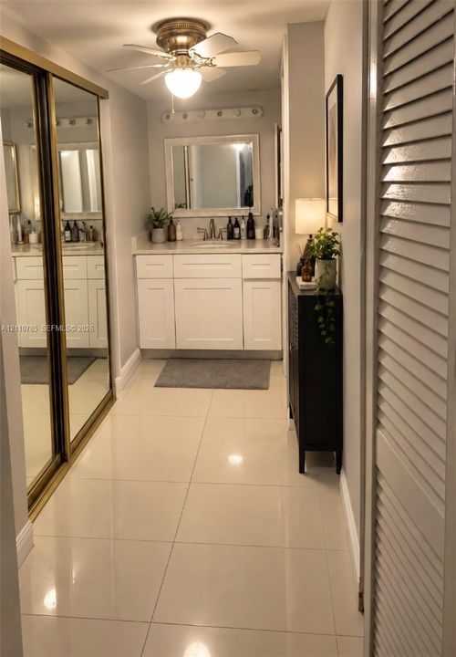 Bathroom featuring a white vanity with a single basin, mirrored sliding-door closet, large-format tile flooring, and wall-mounted vanity mirror
