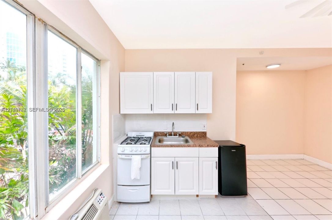 Kitchenette featuring white cabinetry, stone-finish countertops, stainless steel sink with metal faucet, gas range, and tile flooring