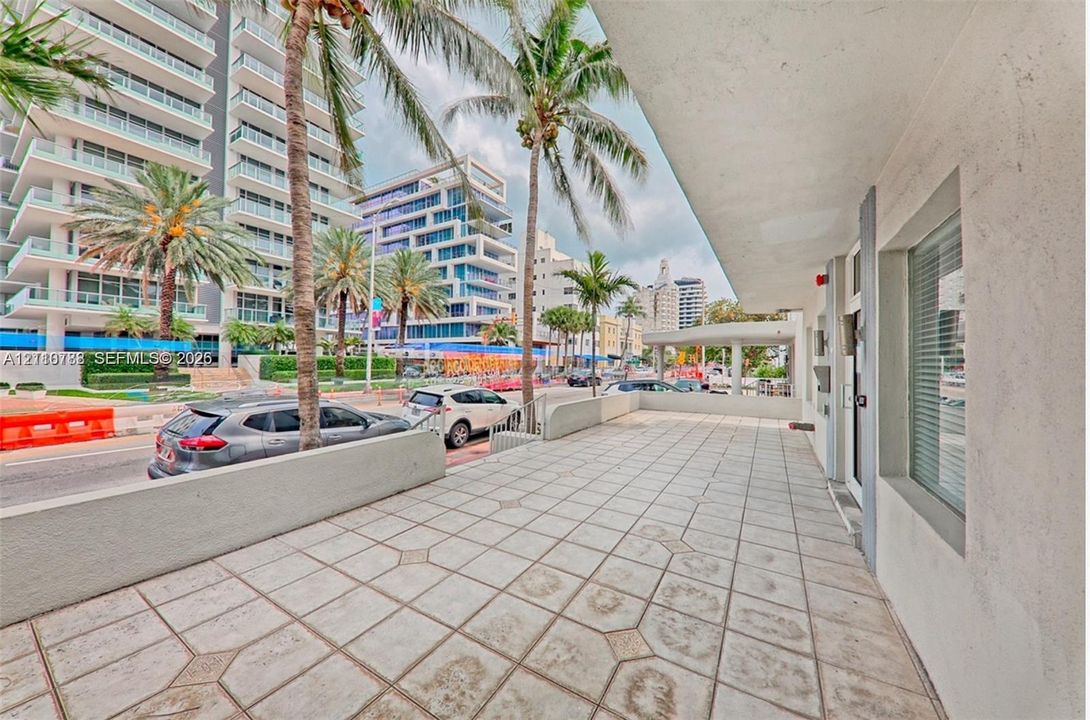 Covered exterior terrace featuring geometric tile flooring, concrete perimeter wall, and built-in glass paneled entry