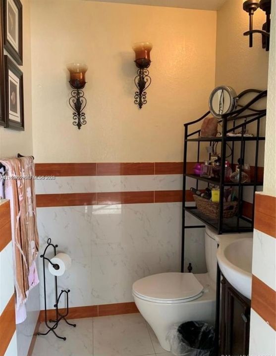 Bathroom featuring patterned wall tile with horizontal stone-finish and wood-finish detailing, floor-to-ceiling tiled walls, pedestal sink, and wall-mounted light fixtures