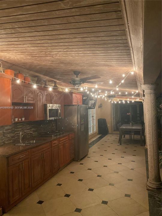 Covered outdoor kitchen featuring wood-plank ceiling, natural stone tile flooring, structural columns, built-in cabinetry, and integrated stainless steel appliances