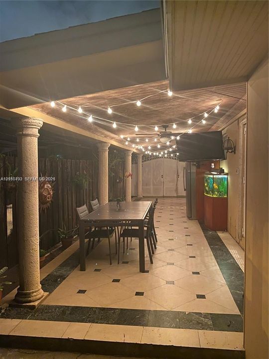 Covered patio featuring concrete columns, tile flooring with decorative inserts, and a built-in ceiling fan